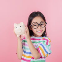 Little Asian girl saving money in a piggy bank, learning about saving, Kid save money for future education. Money, finances, insurance, and people concept